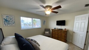 A bedroom with a bed, a ceiling fan, a dresser, a television, and a door. - Westwinds Waterfront Luxury Condo Beach and Pool (Treasure Island)