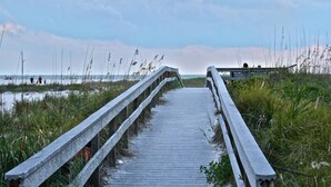 A wooden boardwalk leading to a beach with a railing on one side and tall grasses on the other. - Westwinds Waterfront Luxury Condo Beach and Pool (Treasure Island)