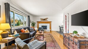 A modern living room with a fireplace, a television, and a large window. - The Mountain Retreat: Steps to Palmer Park, Central COS, Sleeps 8 (Colorado Springs)