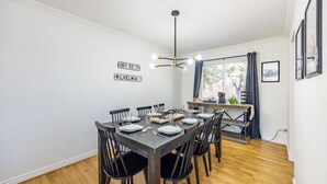 A dining area with a dark wooden table set for six, surrounded by black chairs. There is a modern chandelier above the table, and the room has white walls with two street signs. - The Mountain Retreat: Steps to Palmer Park, Central COS, Sleeps 8 (Colorado Springs)