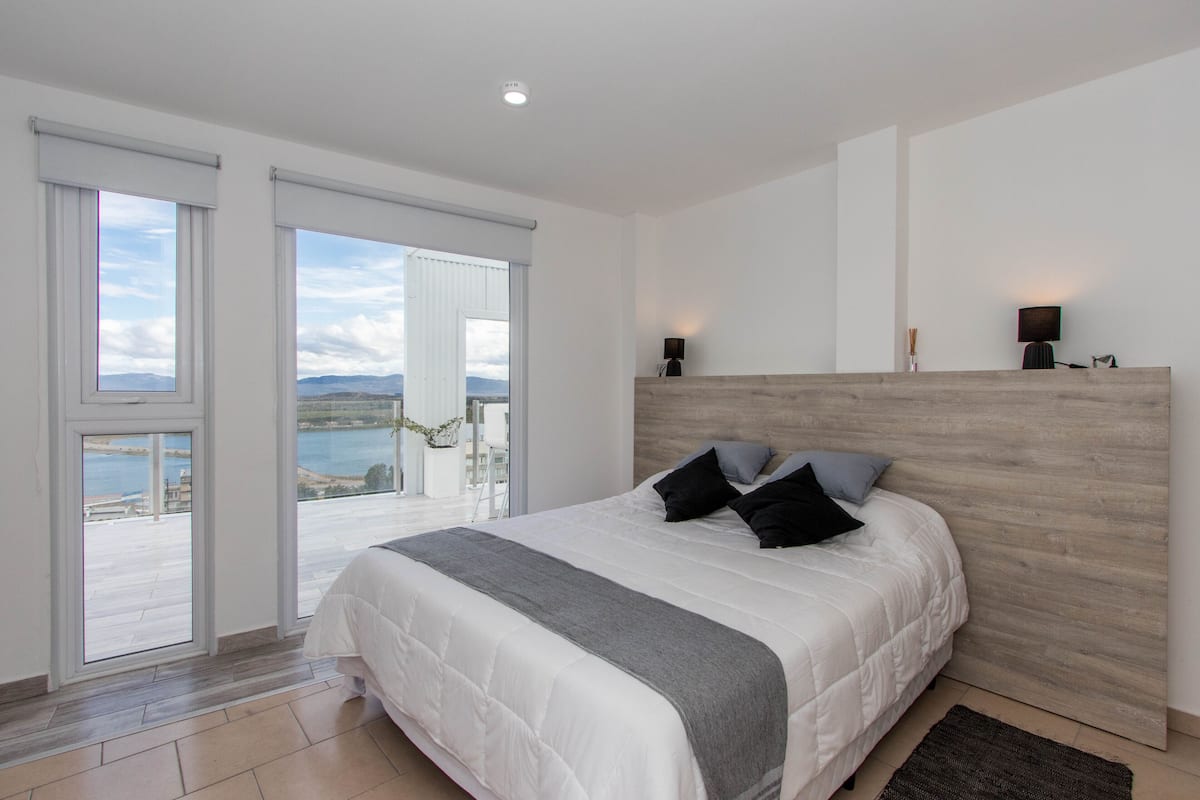 A bedroom with a large bed, a wooden headboard, and a view of the sea through the sliding glass doors.