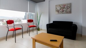 A modern living room with a black sofa, two red chairs, a wooden coffee table, and a painting on the wall.