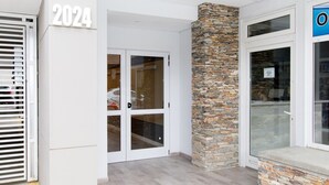 A building entrance with a stone pillar, double glass doors, and a number '2024' sign.