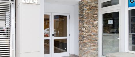 A building entrance with a stone pillar, double glass doors, and a number '2024' sign.
