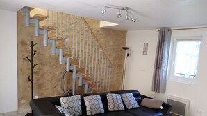 Een woonkamer met een zwarte leren bank, decoratieve kussens, een trap en een vloerlamp.