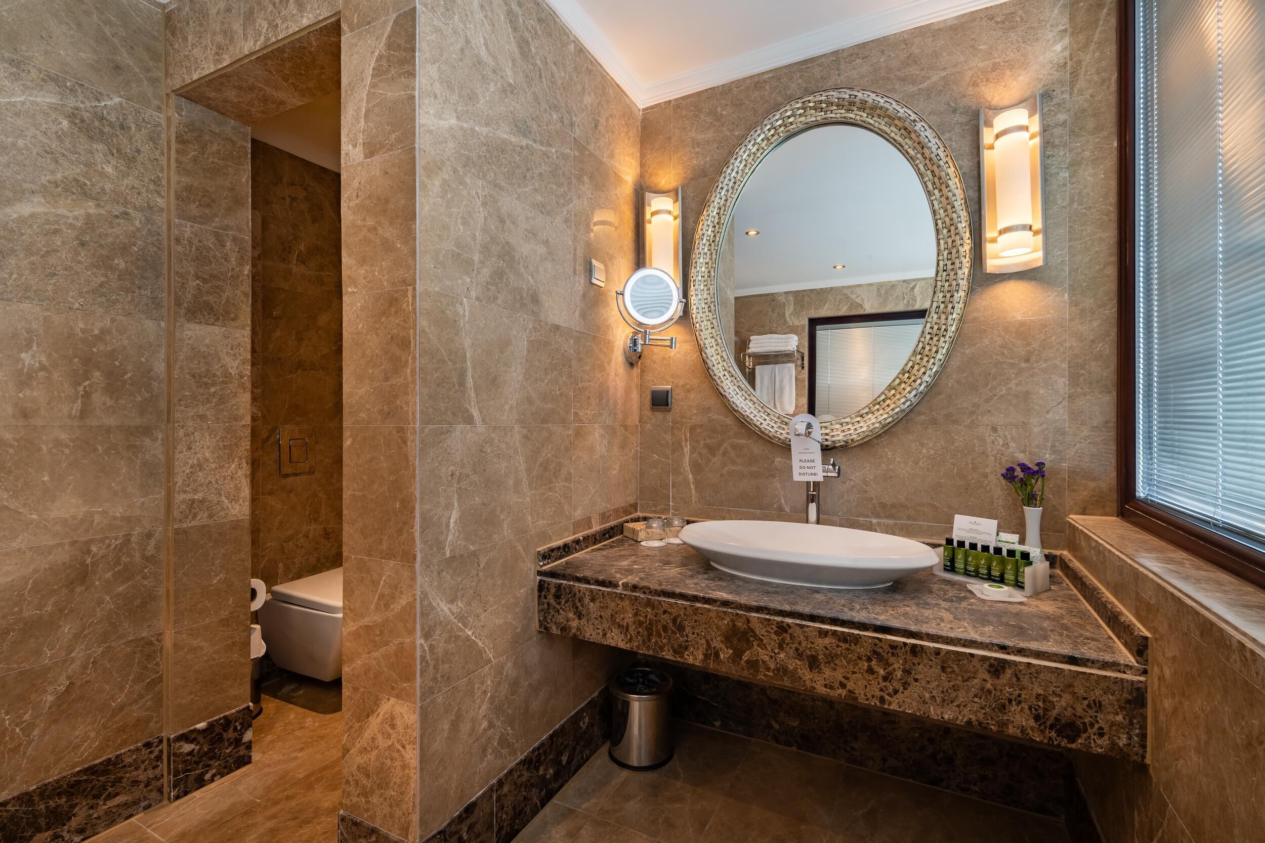 A modern bathroom with a marble vanity, a large mirror, and a toilet visible in the background.
