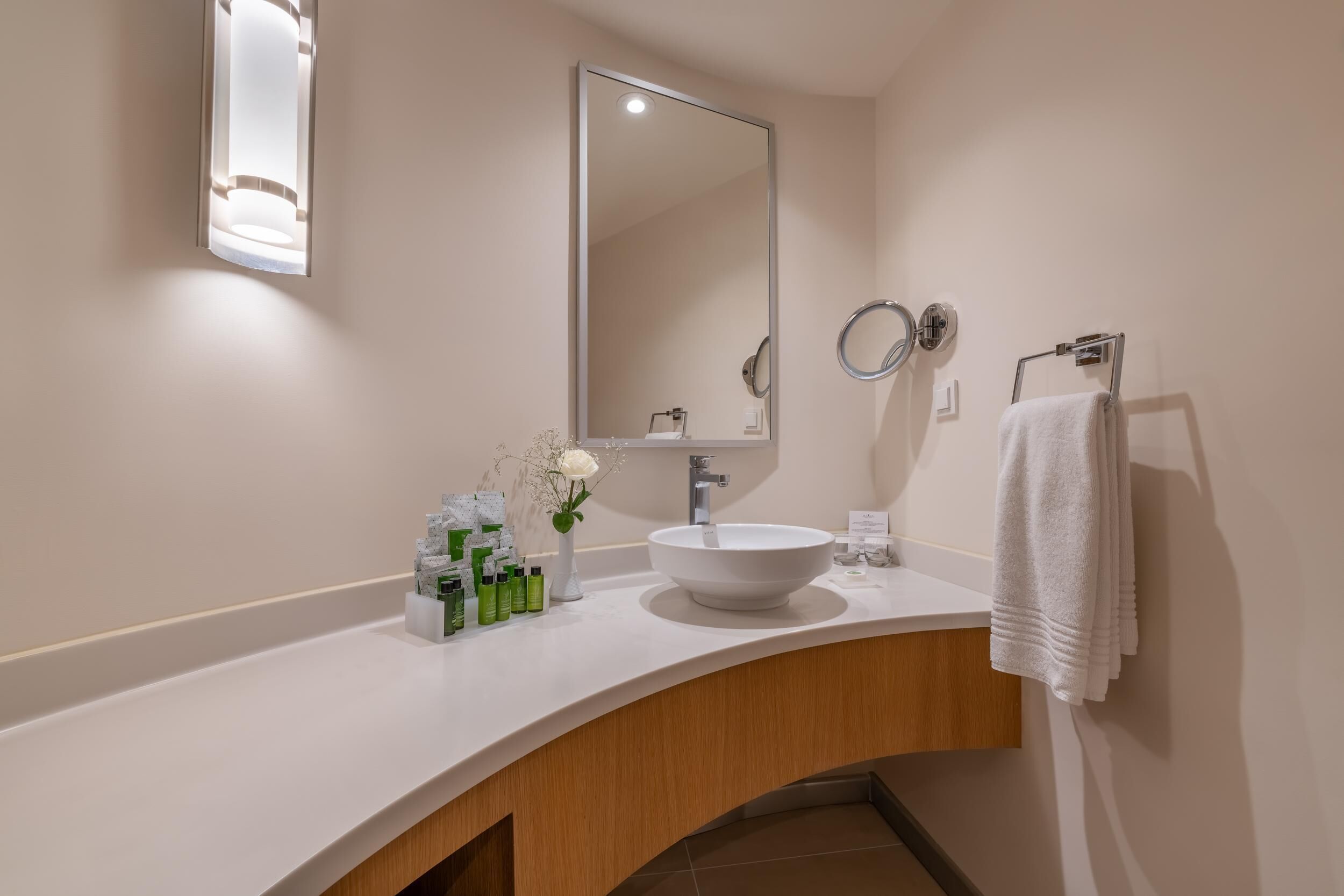 A modern bathroom with a white sink, a large mirror, and a towel rack.