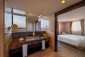 A modern bathroom with a marble sink, a large mirror, and a separate bedroom with a bed and curtains.