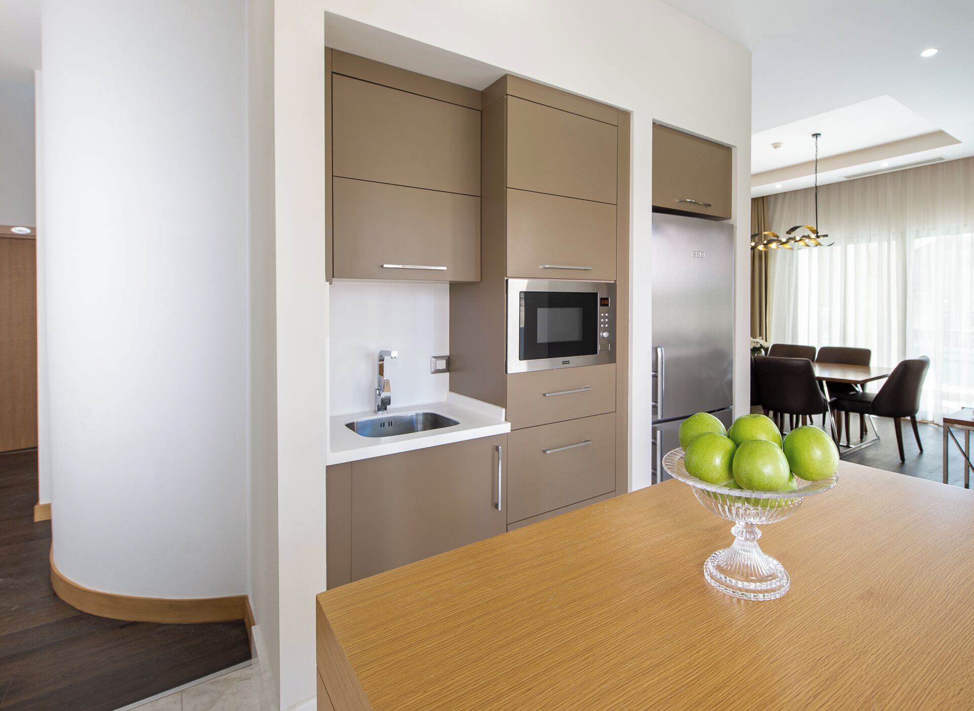 Een moderne keuken met inbouwapparatuur, een houten eettafel met een fruitschaal, en een zithoek met stoelen.