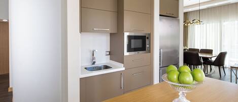 Een moderne keuken met inbouwapparatuur, een houten eettafel met een fruitschaal, en een zithoek met stoelen.