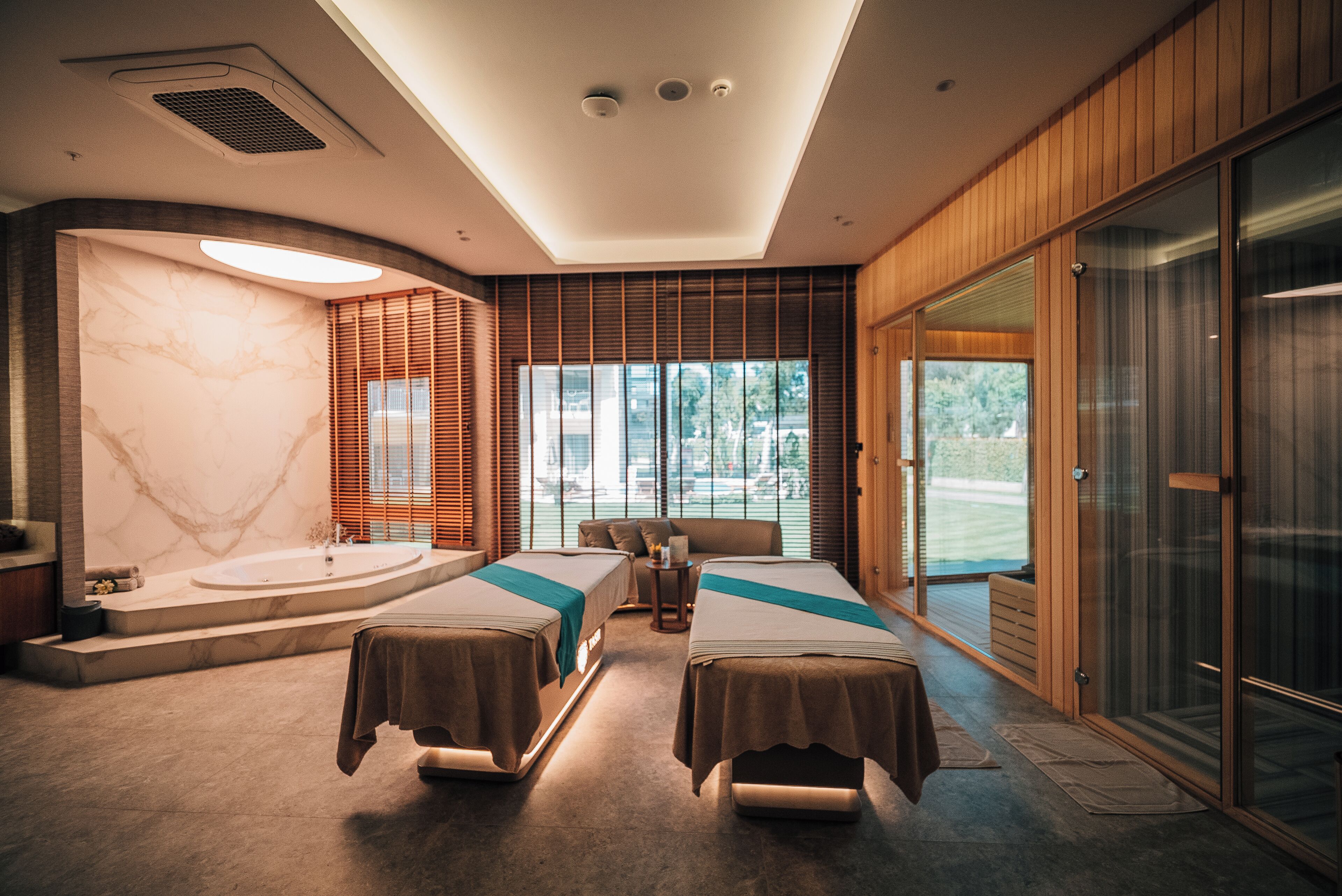 A modern spa room with two beds, a large window, a bathtub, and a sliding glass door.