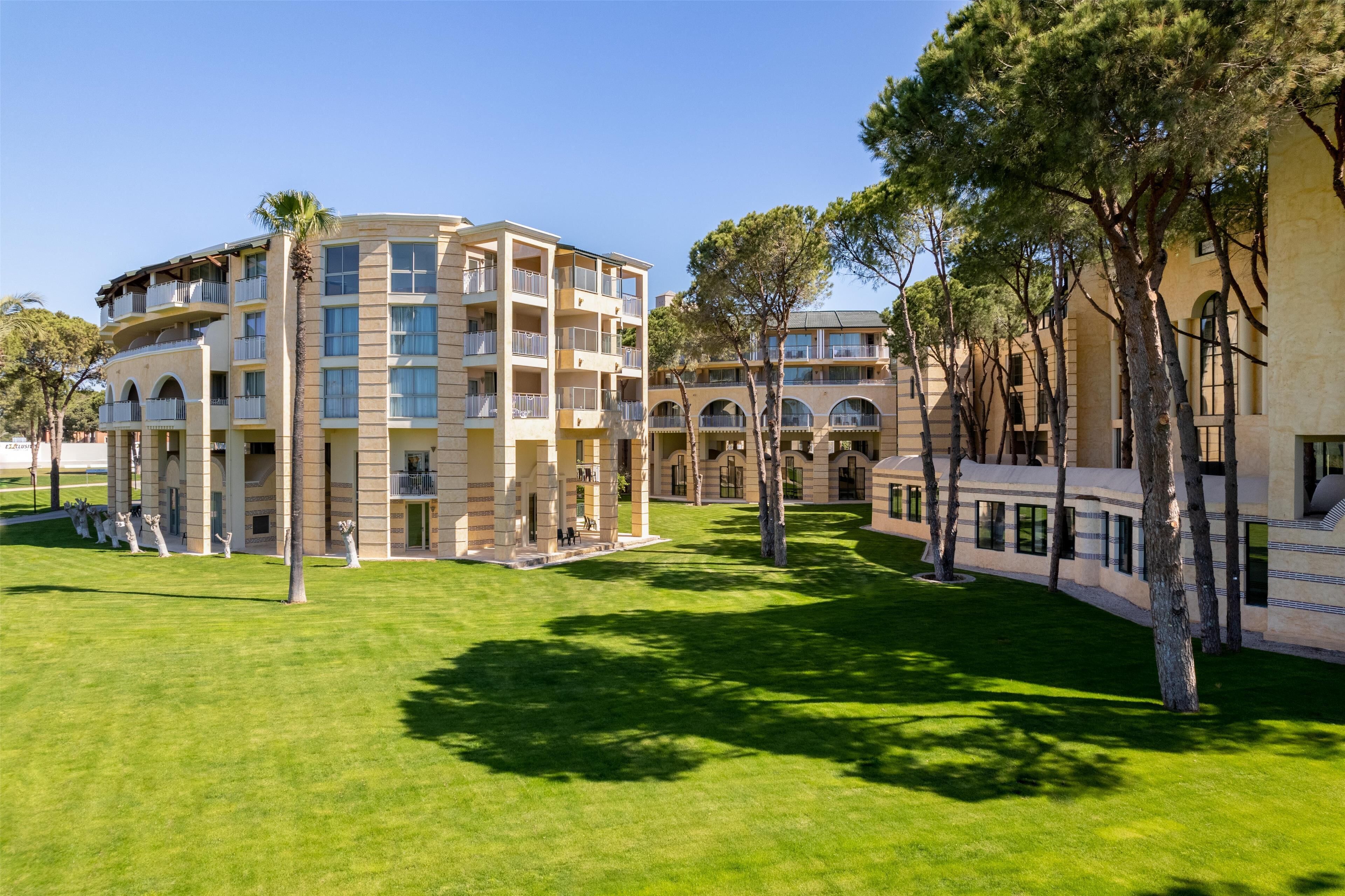 Un hotel de varios pisos con balcones, un patio y árboles.