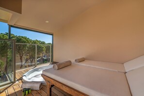 A balcony with a bed, a glass door, and bottles of water.