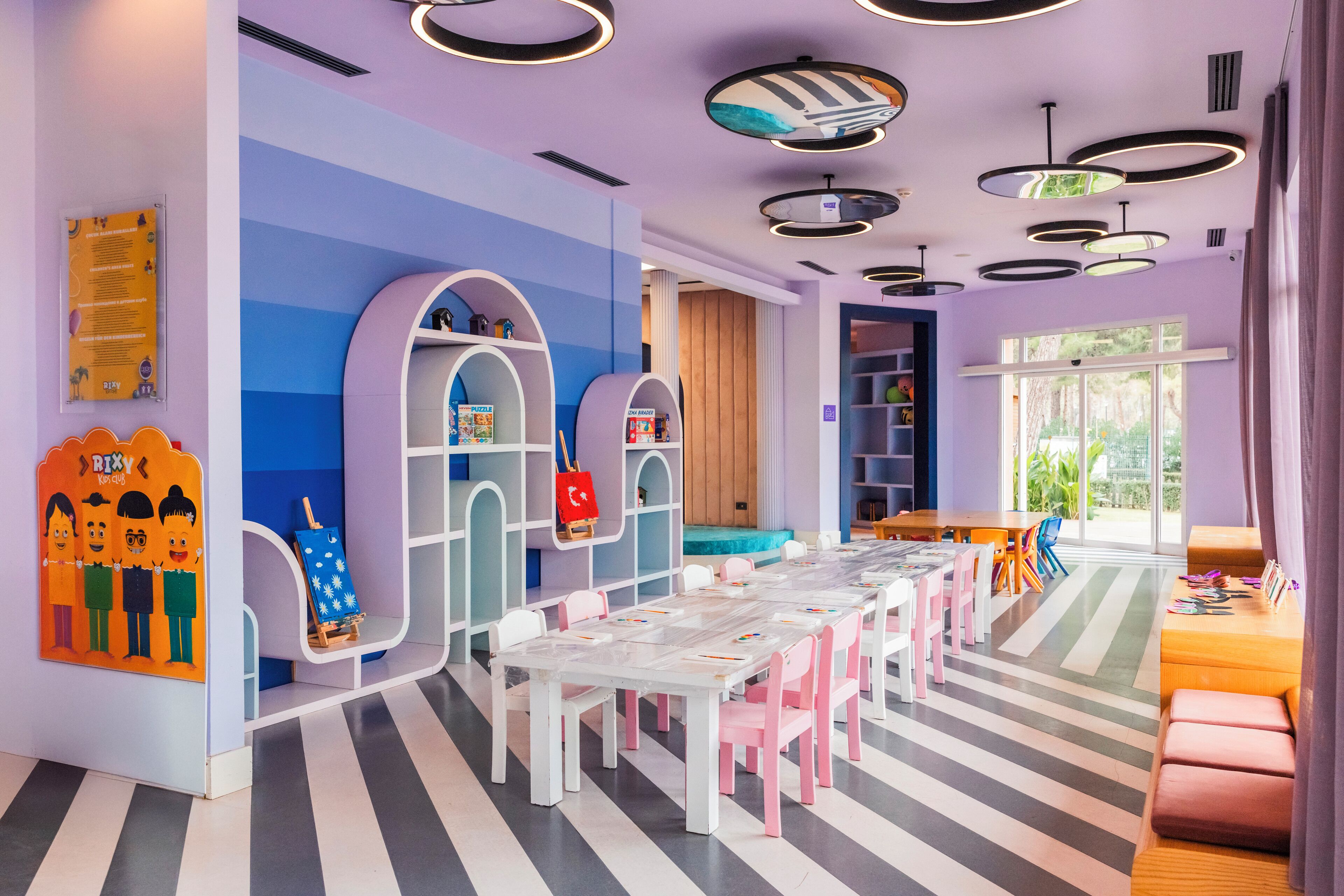 A children's playroom with a long table, chairs, and colorful storage units.