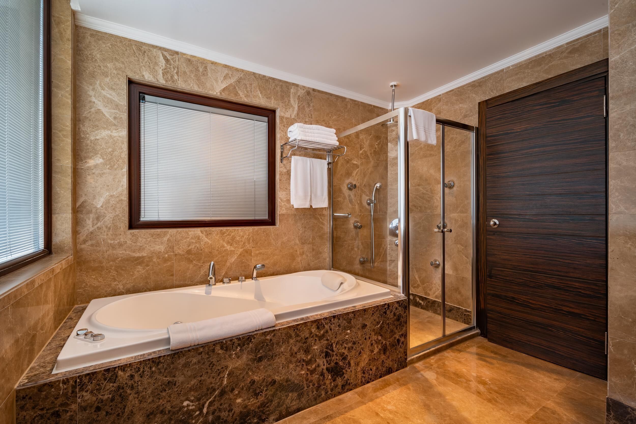 A modern bathroom with a large bathtub, a glass shower enclosure, and a dark wooden door.
