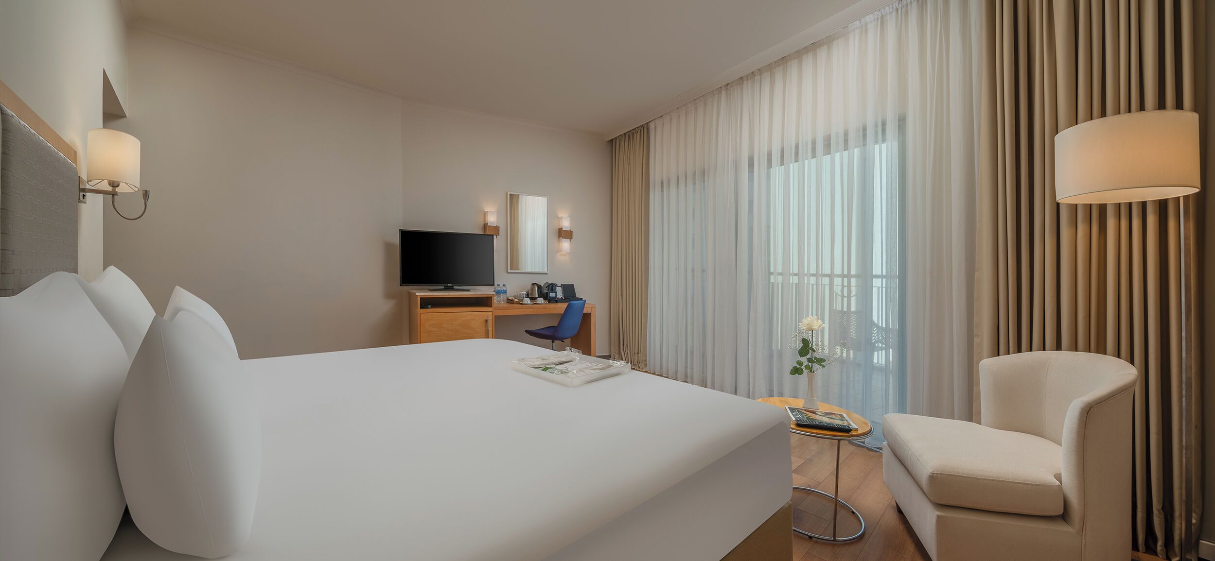 A hotel room with a large bed, a desk with a TV, a chair, and a window with curtains.