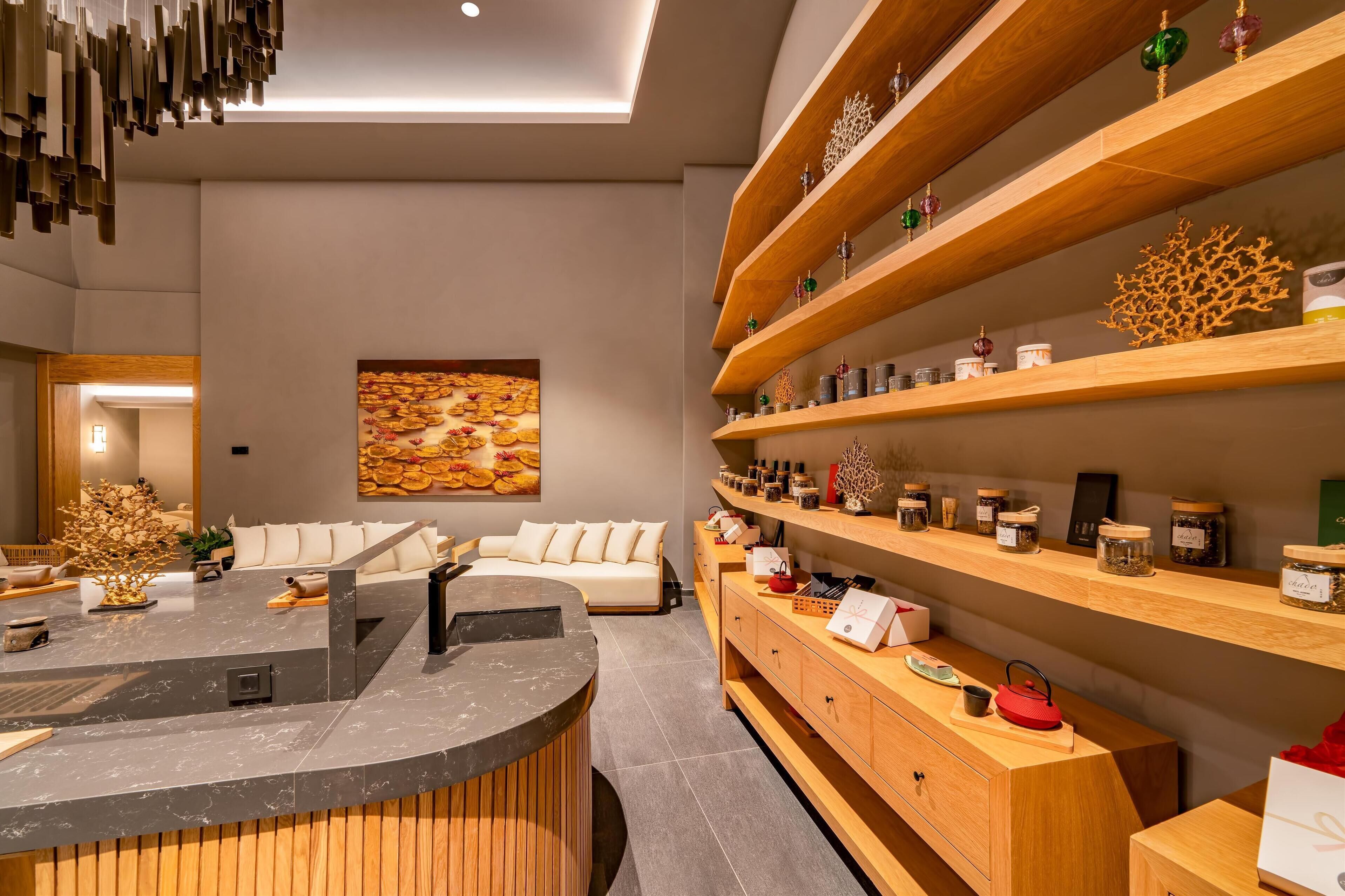 Un moderno vestíbulo de hotel con una recepción, un sofá y estantes de madera con frascos y objetos decorativos.