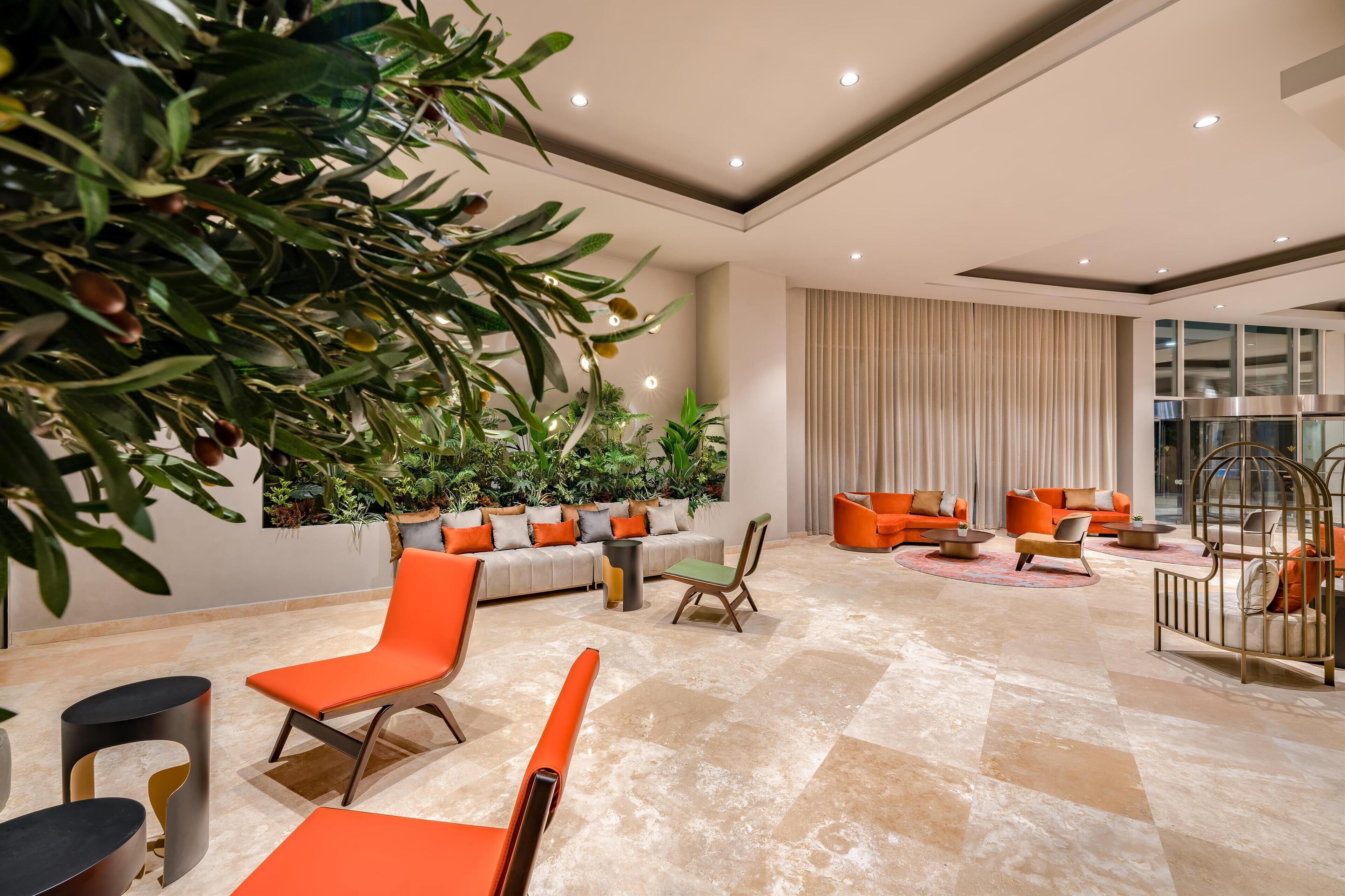 A modern lounge area with orange seating, a large potted plant, and a decorative metal chair.