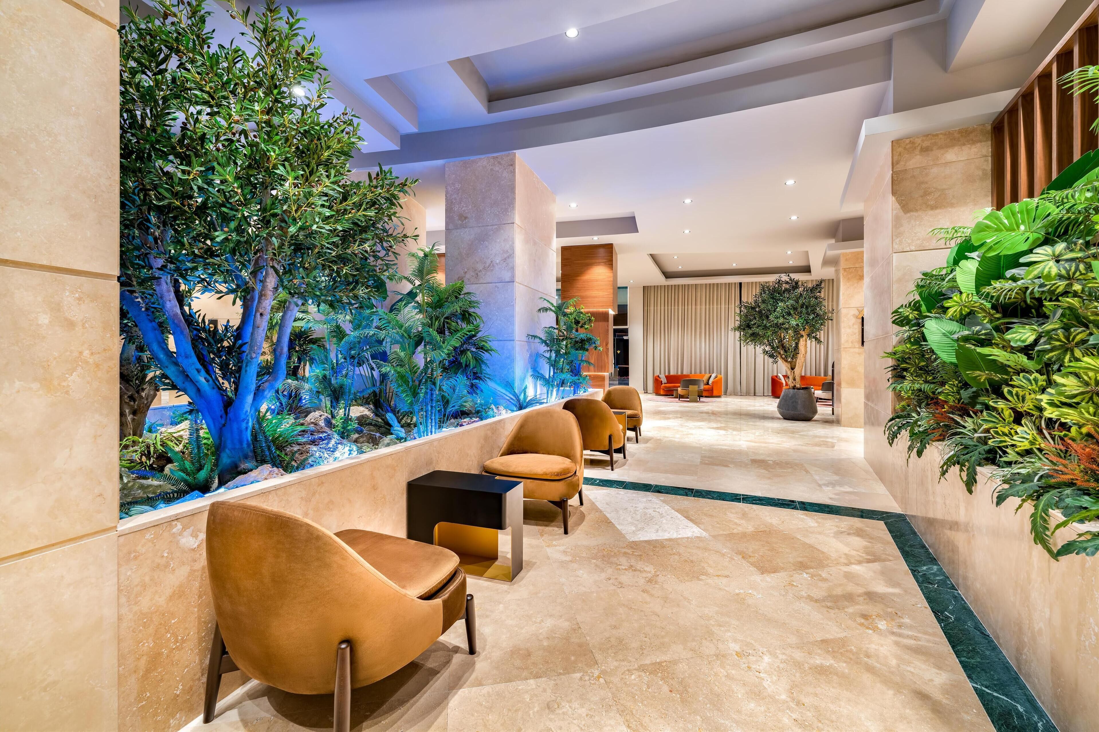 Un hall d’entrée moderne doté d’un espace salon, d’un élément décoratif aquatique et d’une végétation luxuriante.
