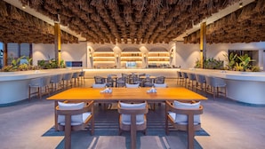 A spacious indoor area with a long wooden table surrounded by chairs, a bar area with shelves of bottles, and a ceiling covered with hanging thatch. - Rixos Park Belek - All Inclusive - The Land of Legends Access (Serik)