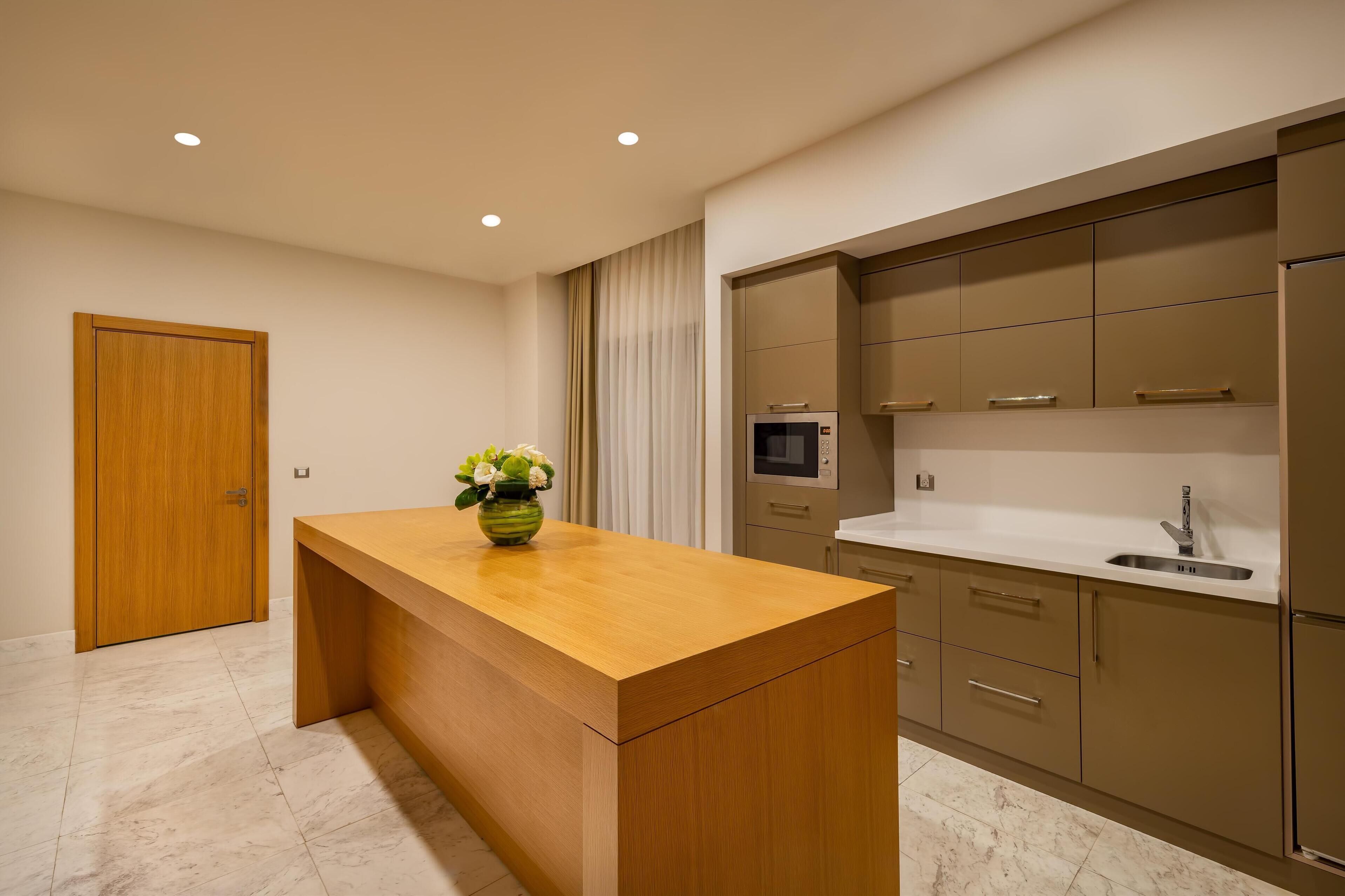 A modern kitchen with a wooden island, built-in appliances, and a marble floor.