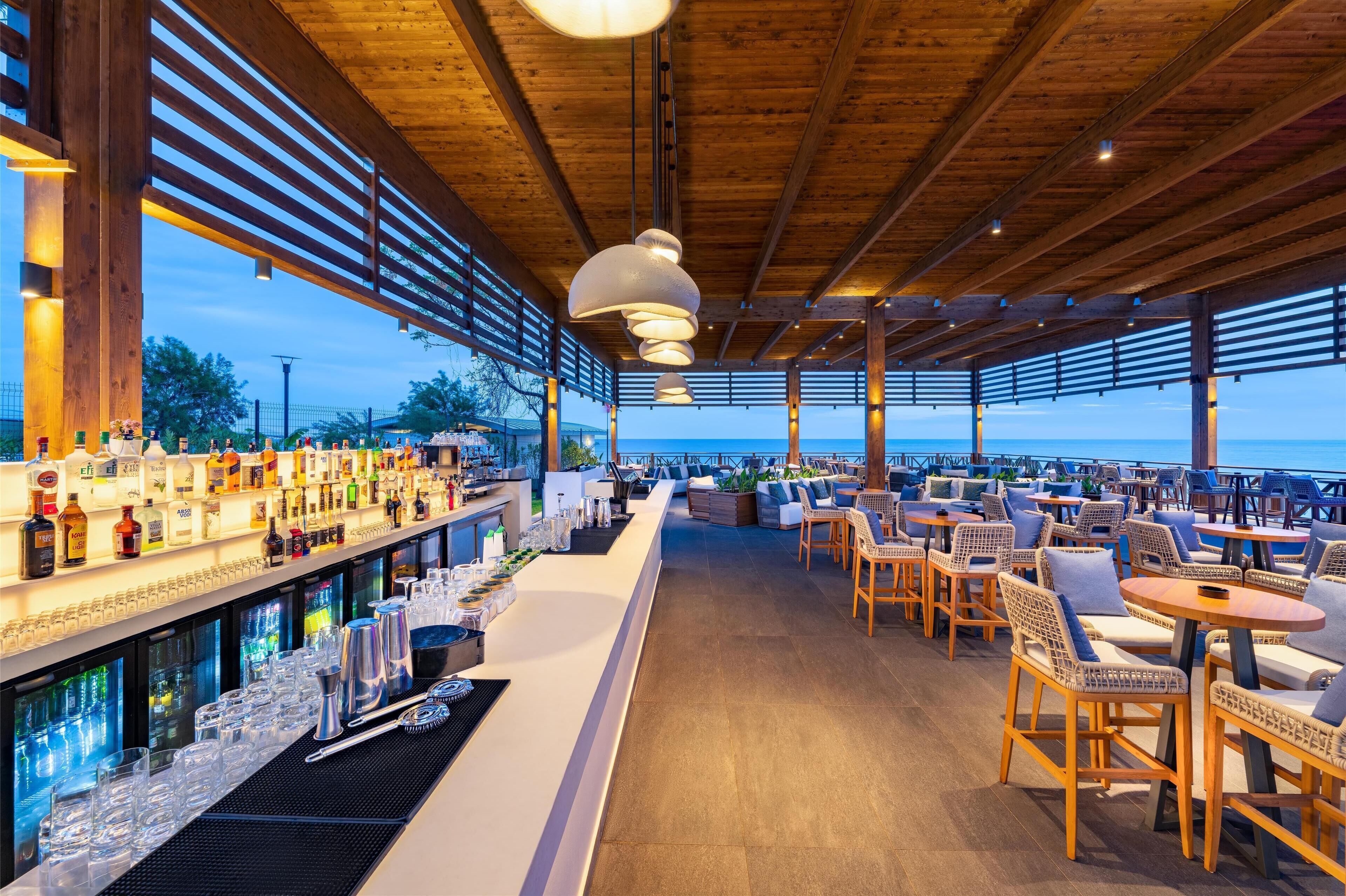 A rooftop bar with a long counter, bar stools, and a view of the sea.