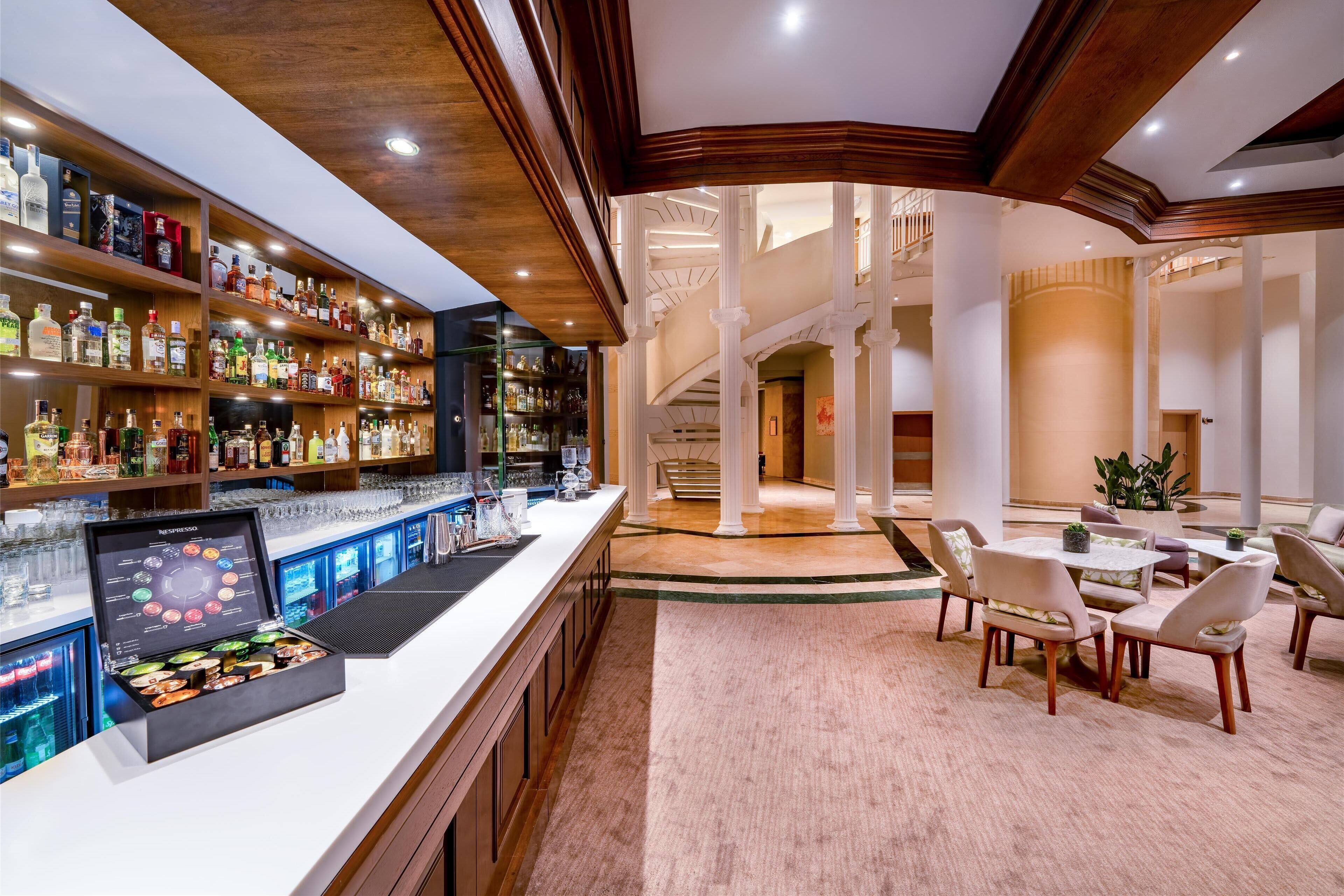 A bar area with shelves of liquor bottles, a digital menu display, and a seating area with tables and chairs.