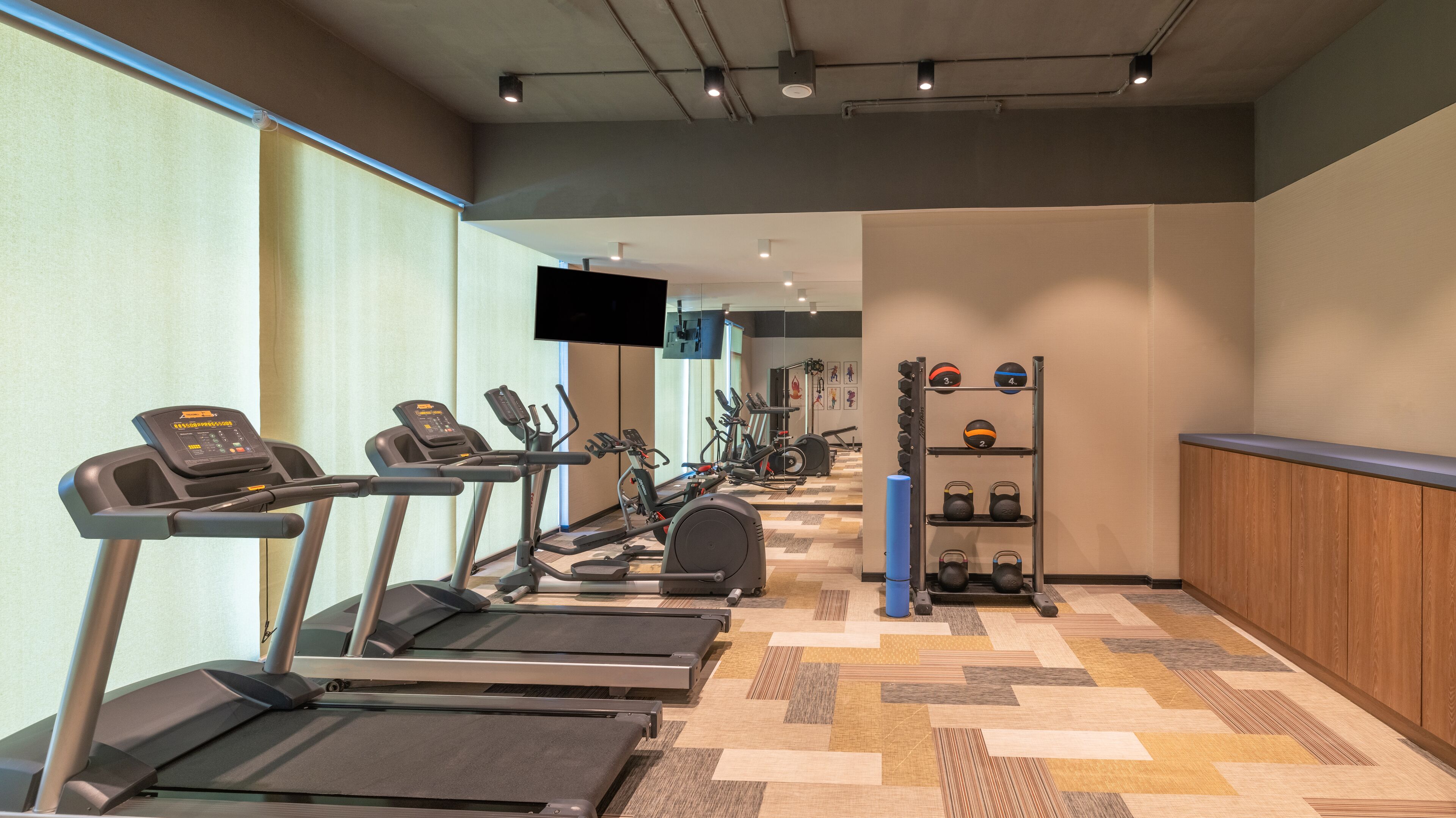 A gym with treadmills, elliptical machines, and a weight rack.