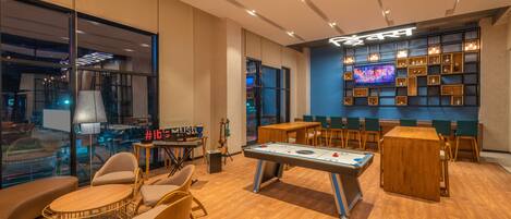 A cozy bar area with a pool table, comfortable seating, and a TV screen displaying a music video.