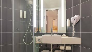 A modern bathroom with a glass-enclosed shower, a white sink with a mirror above it, and a hairdryer mounted on the wall.