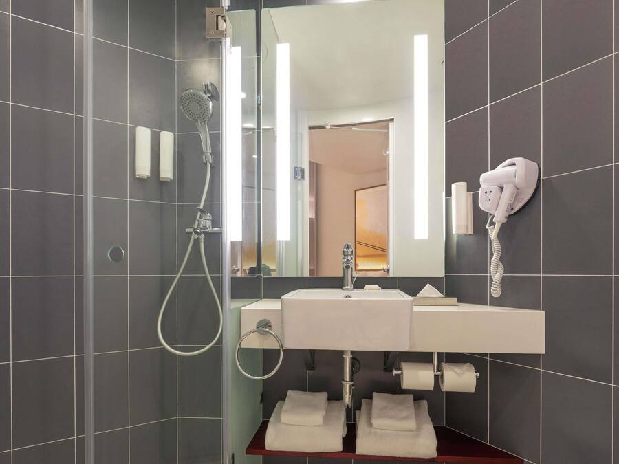 A modern bathroom with a glass-enclosed shower, a white sink with a mirror above it, and a hairdryer mounted on the wall.
