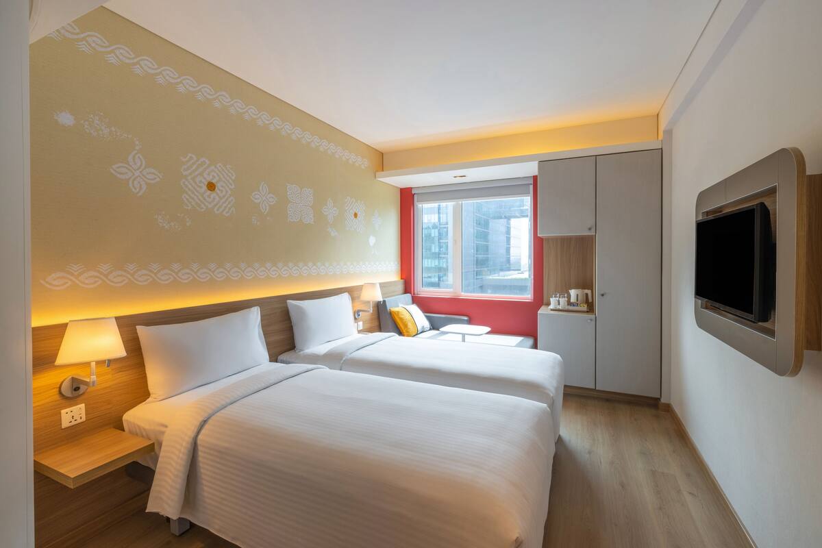 A hotel room with two beds, a TV, a window, and a minibar.