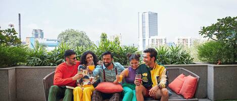 A group of people sitting on a bench outdoors with a cityscape in the background.