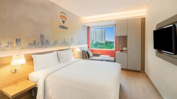 A hotel room with a large bed, a desk, a chair, a TV, and a window with a cityscape view.