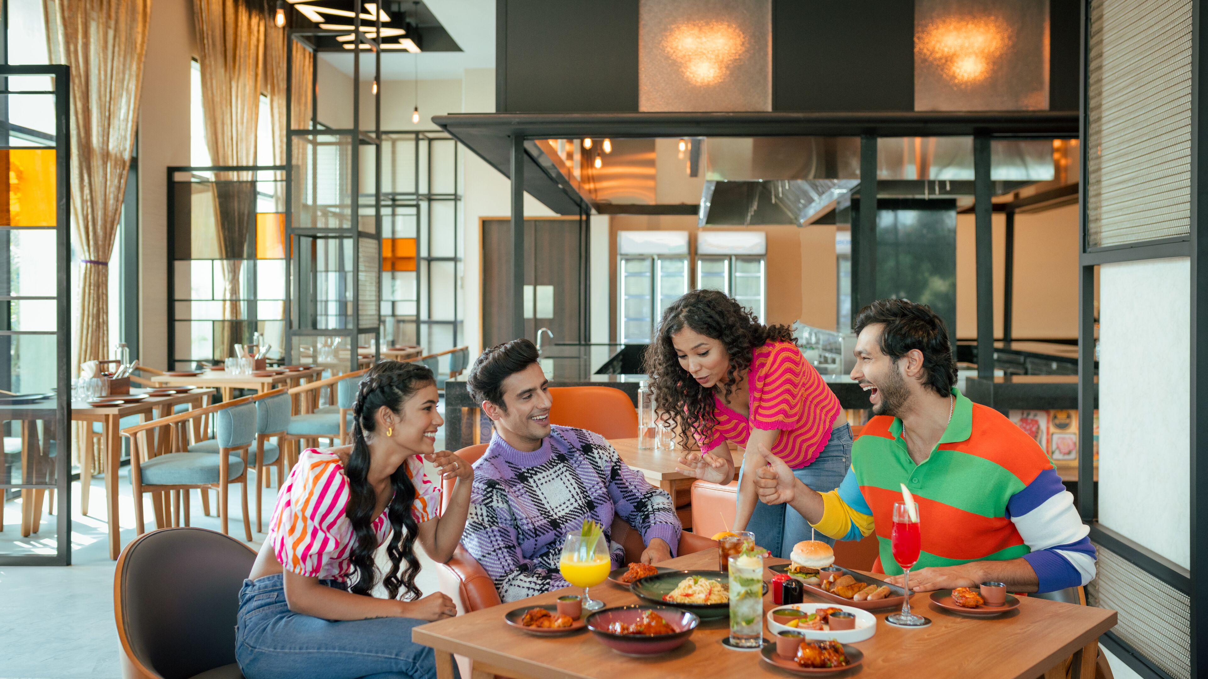 A group of people dining at a restaurant with a modern interior, large windows, and a variety of dishes on the table.