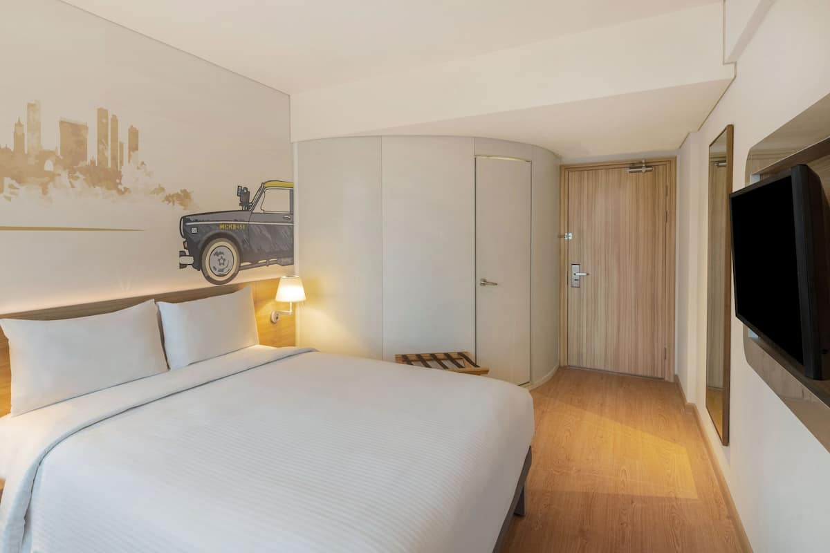 A hotel room with a bed, nightstands, a wall-mounted TV, a wardrobe, and a cityscape mural.