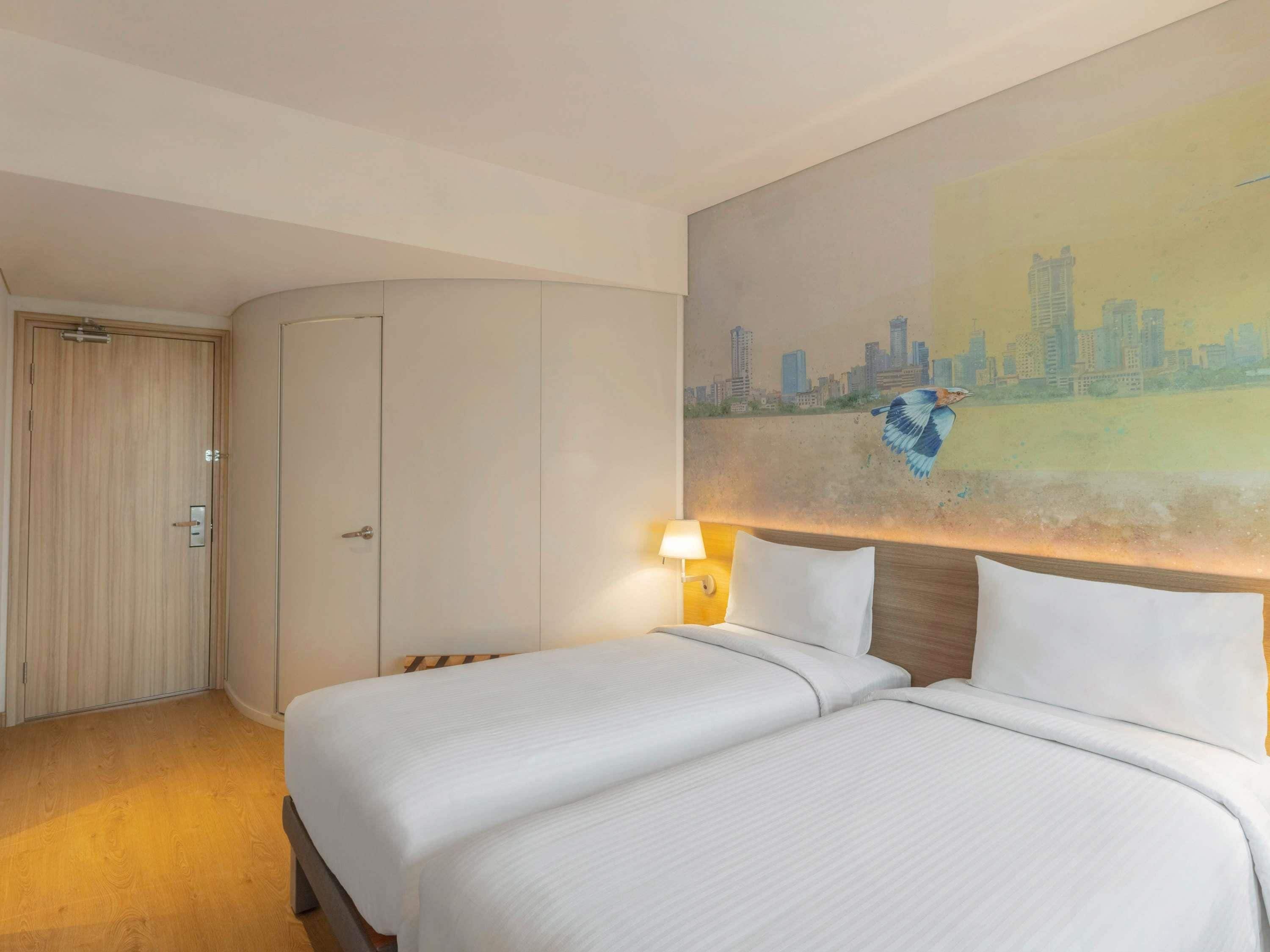 Habitación de hotel con dos camas, un cuadro de paisaje urbano, un armario de madera y una lámpara.