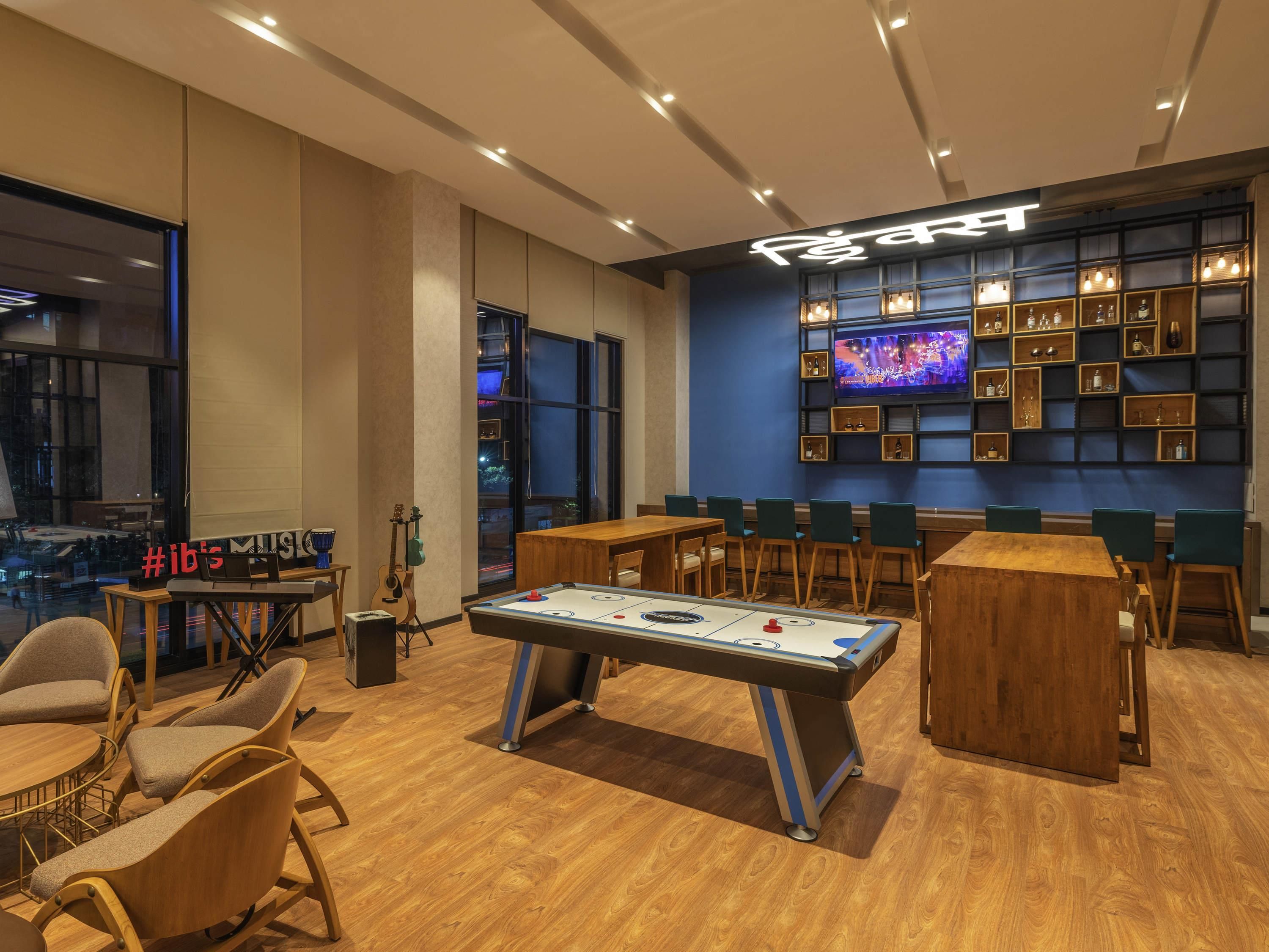 Un espacio interior moderno con mesa de futbolín, asientos, televisor y una zona de bar con estantes.