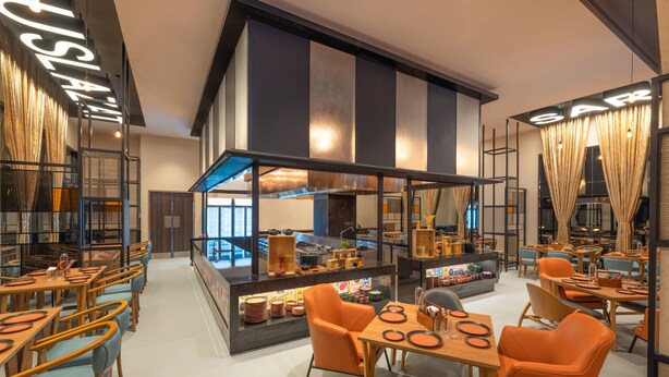 A restaurant with a central counter, multiple tables, and chairs. - Ibis Thane (Thane)