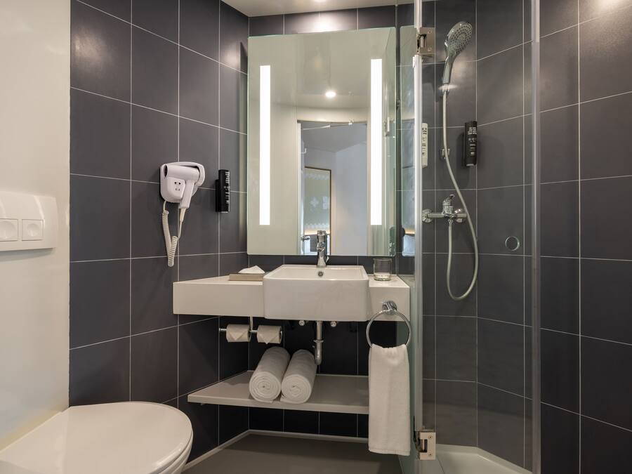Un baño moderno con inodoro blanco, un lavabo con espejo encima y una ducha con cabezal de ducha manual, además de un perchero para toallas.