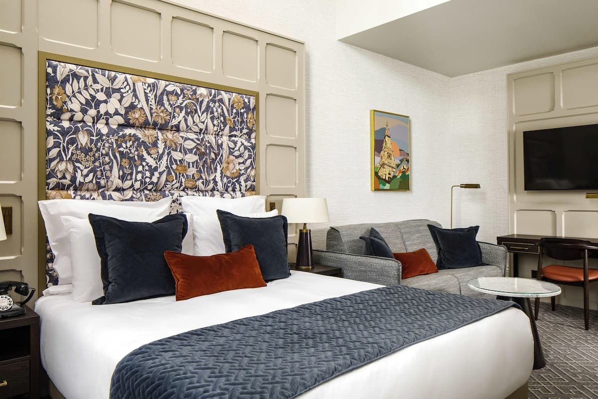 A hotel room with a large bed, a sofa, a desk, and a TV.