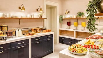 Montaje de bufé con diversos alimentos y bebidas, incluyendo frutas, pasteles y una selección de refrescos.