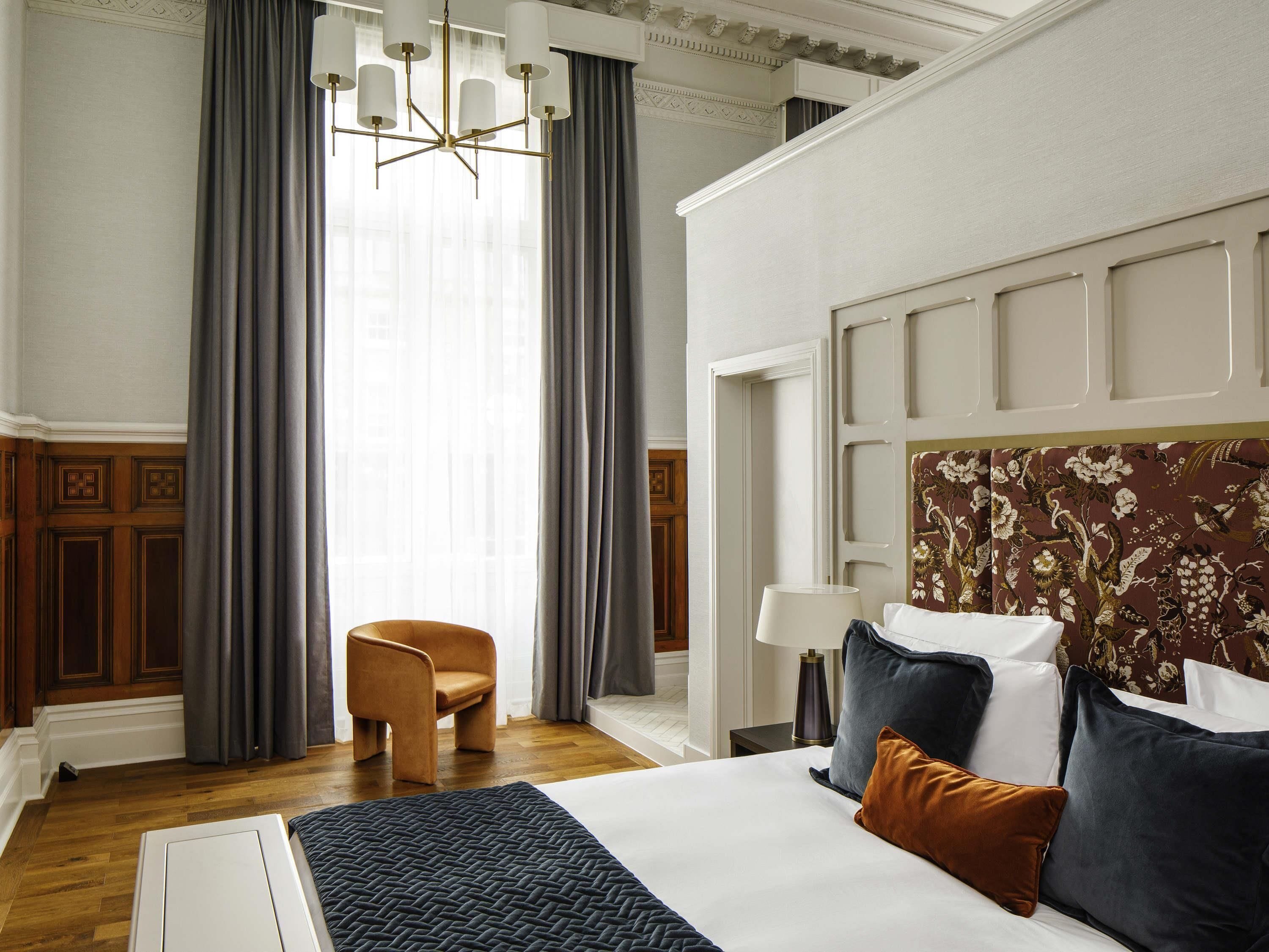A hotel room with a large bed, a chair, a desk, and a chandelier.