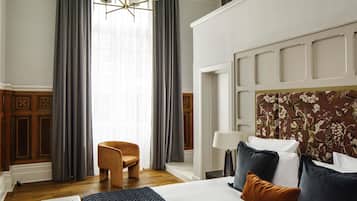 A hotel room with a large bed, a chair, a desk, and a chandelier.