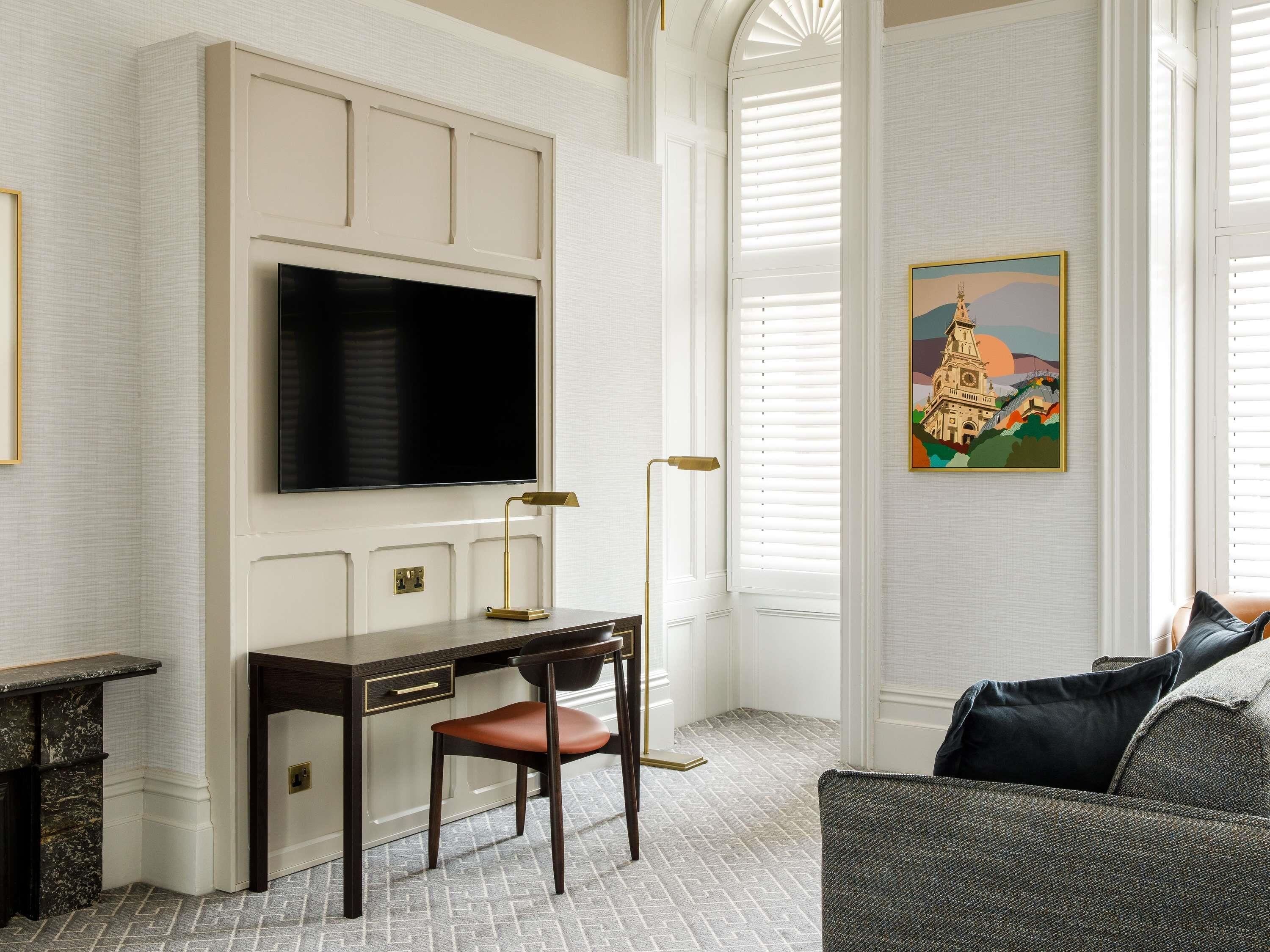 A room with a desk, chair, TV, floor lamp, and a painting.