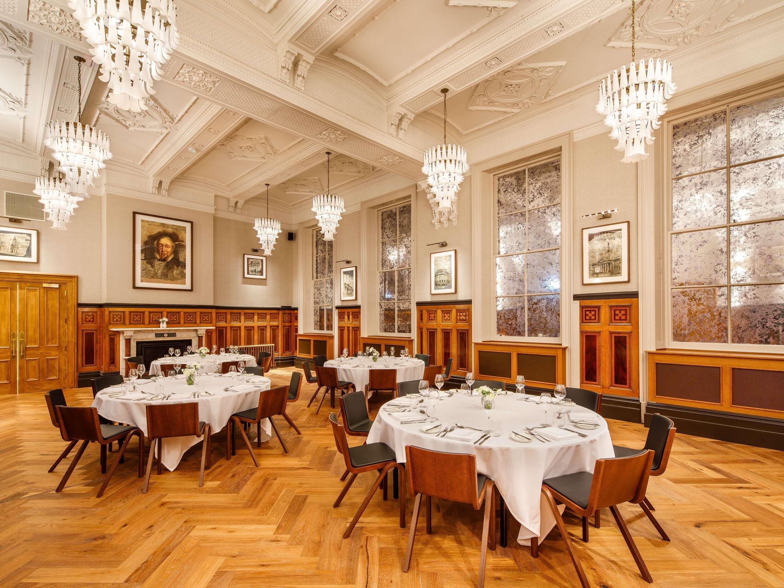 A formal dining room with multiple round tables, chandeliers, and framed artwork on the walls.