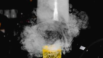 A person pouring a drink from a shaker into a glass, surrounded by smoke.