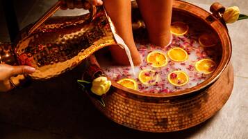 A copper basin filled with a bubbling liquid, garnished with orange slices and flowers, with a person pouring from a patterned bowl.