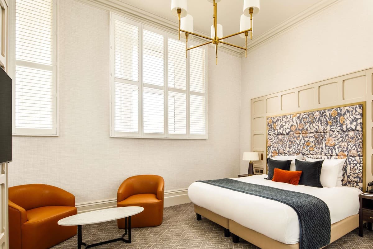 A hotel room with a large bed, two armchairs, a small table, and a decorative headboard.
