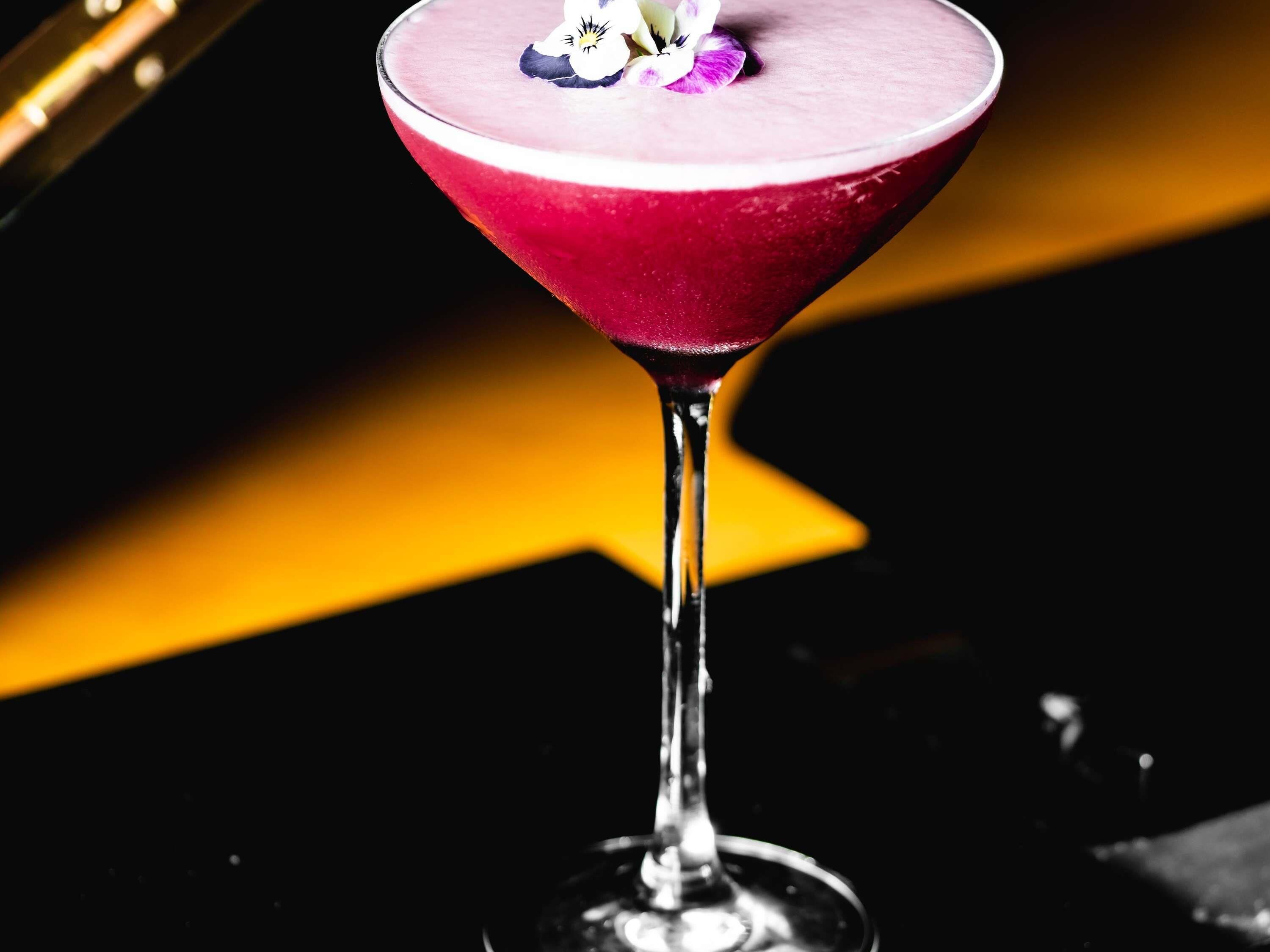 A martini glass with a pink drink and a flower garnish.